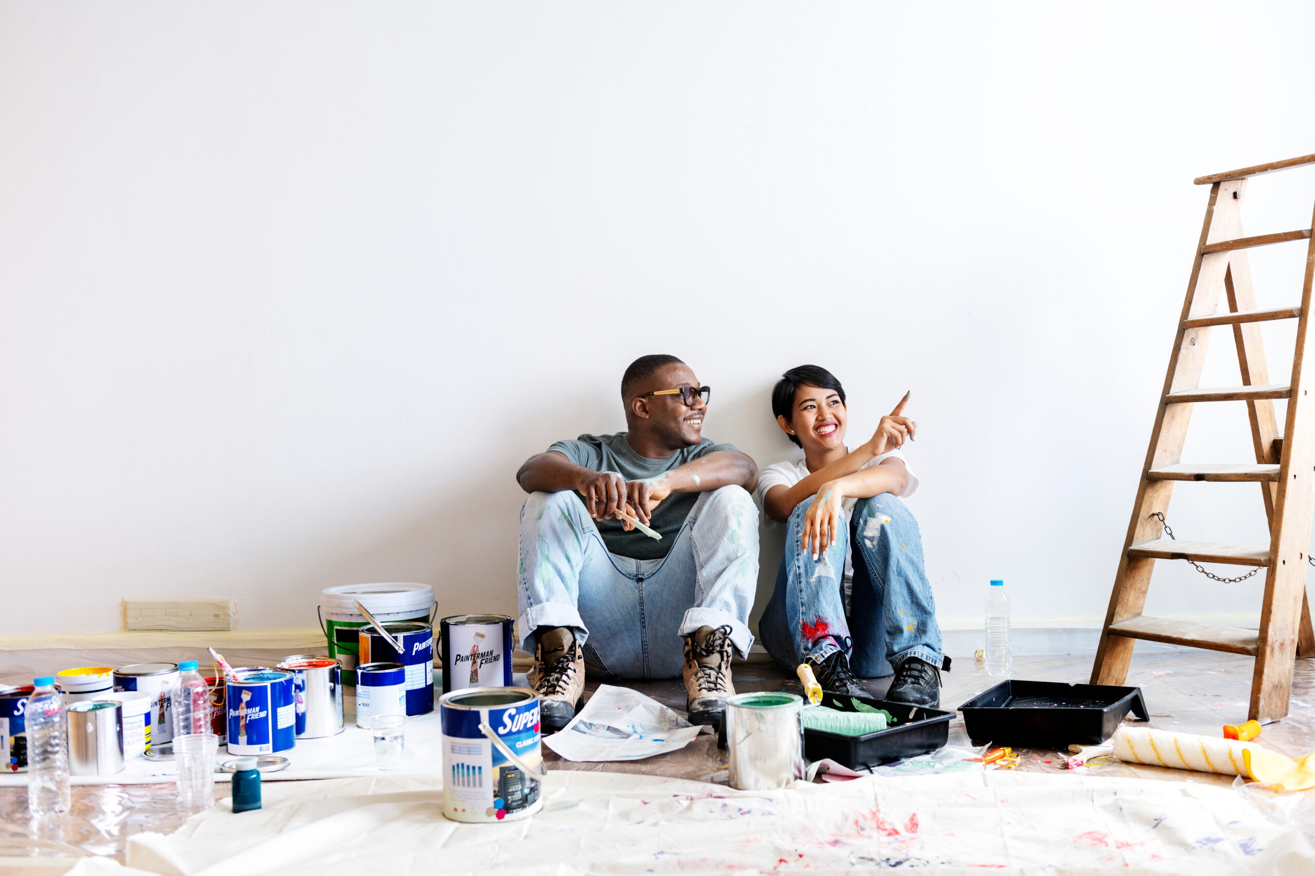 A photograph showing a discussion between a seated man and woman, next to paint tins and some ladders